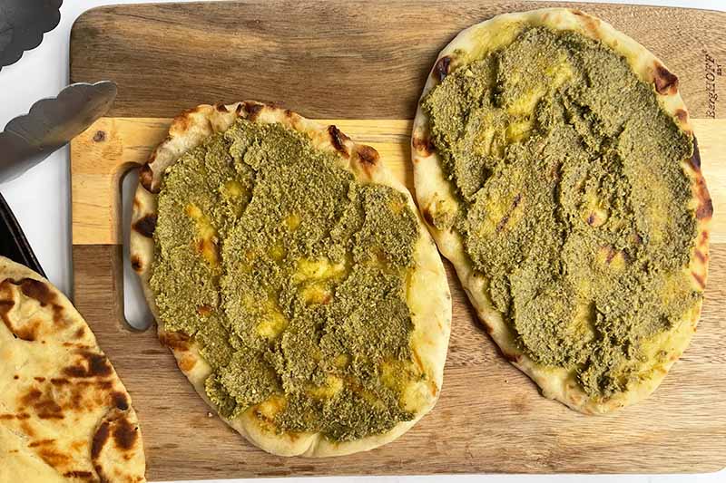 Horizontal image of pesto spread on naan on a wooden board.
