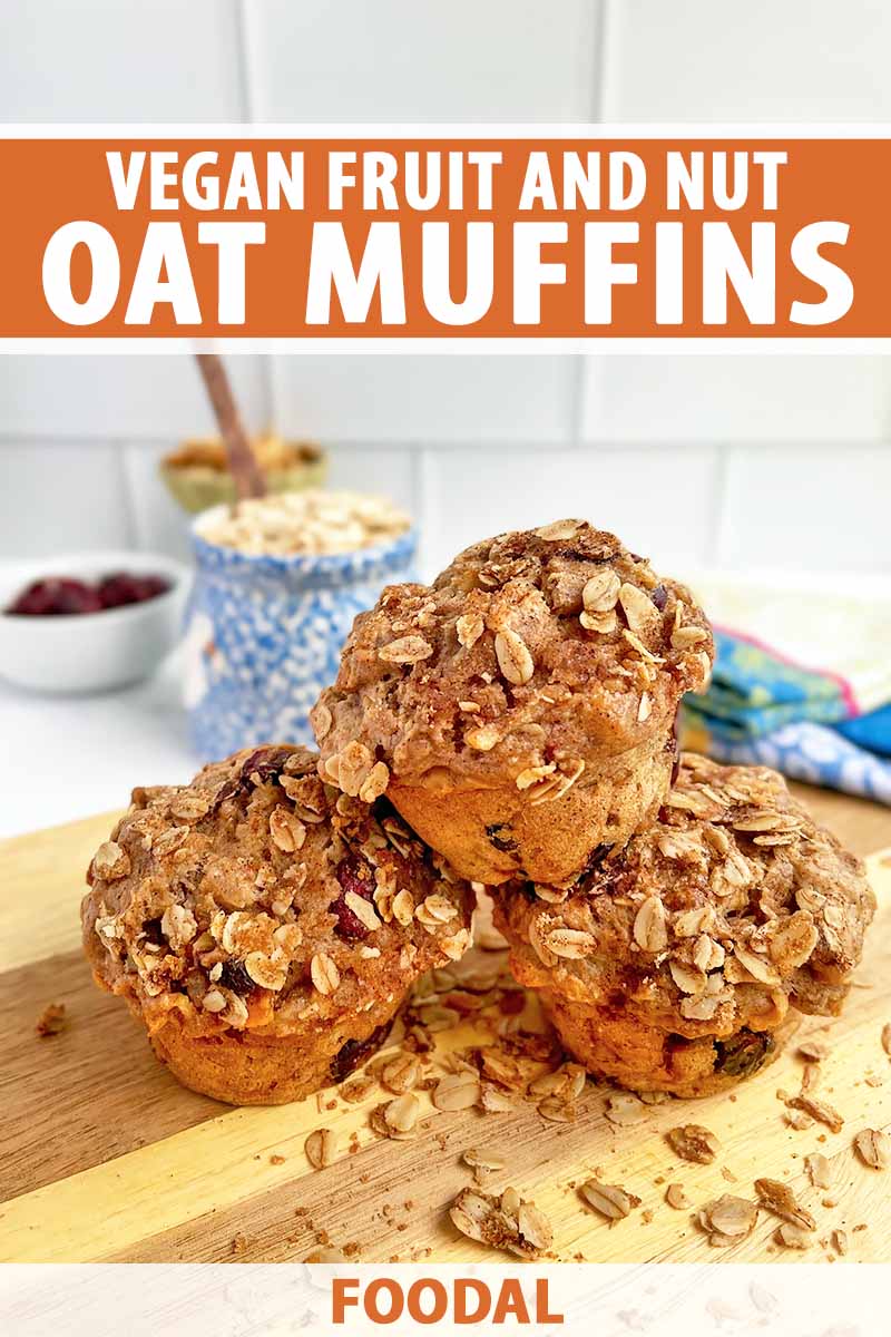Vertical image of a small stack of muffins with an oat crumble topping on a wooden cutting board in front of bowls of nuts and dried fruit, with text on the top and bottom of the image.
