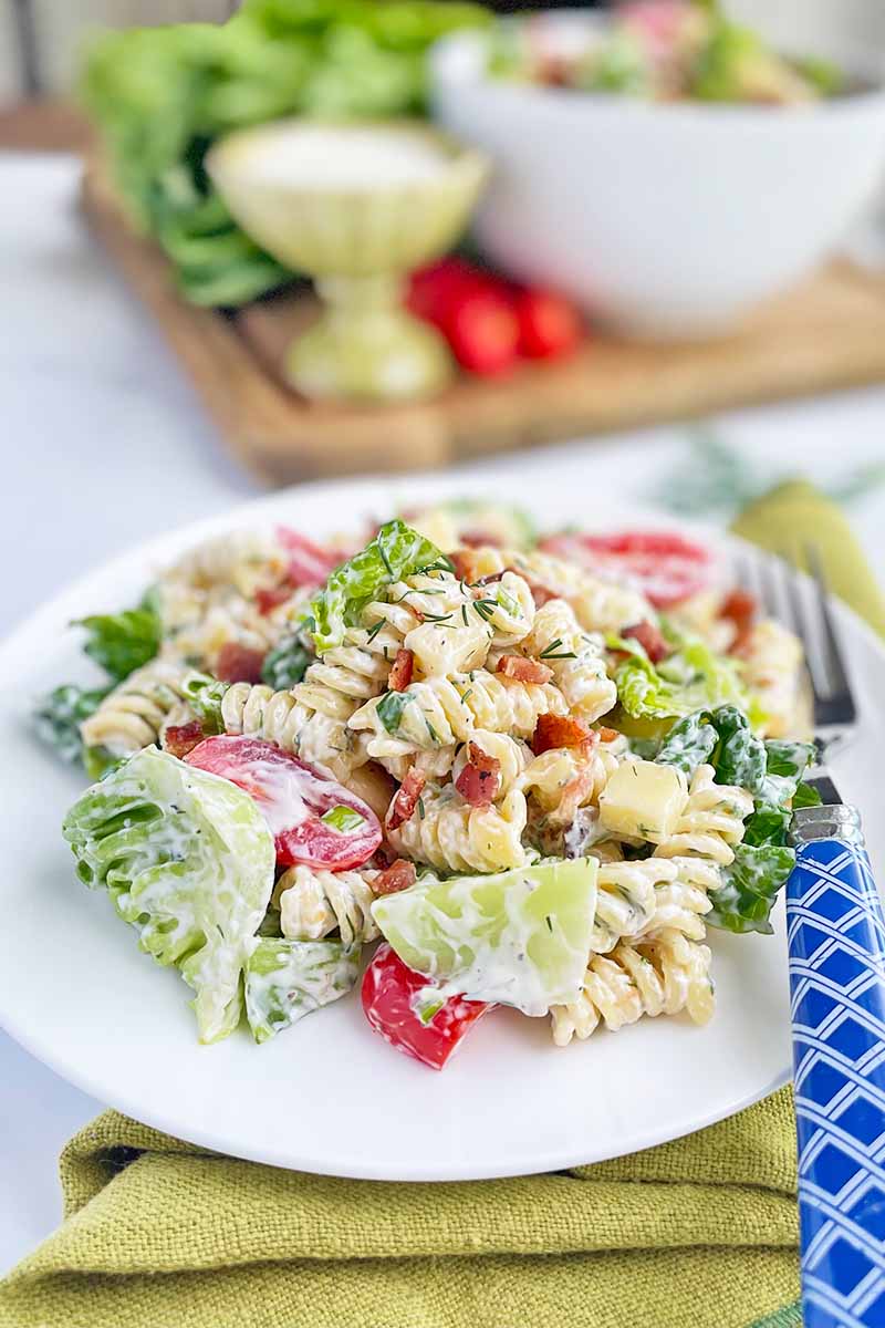 Vertical image of a white plate with a large serving of pasta salad with a blue fork on a green napkin.
