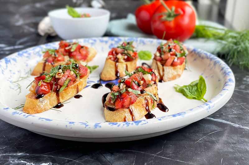 Horizontal image of a platter with bruschetta drizzled with a dark glaze.
