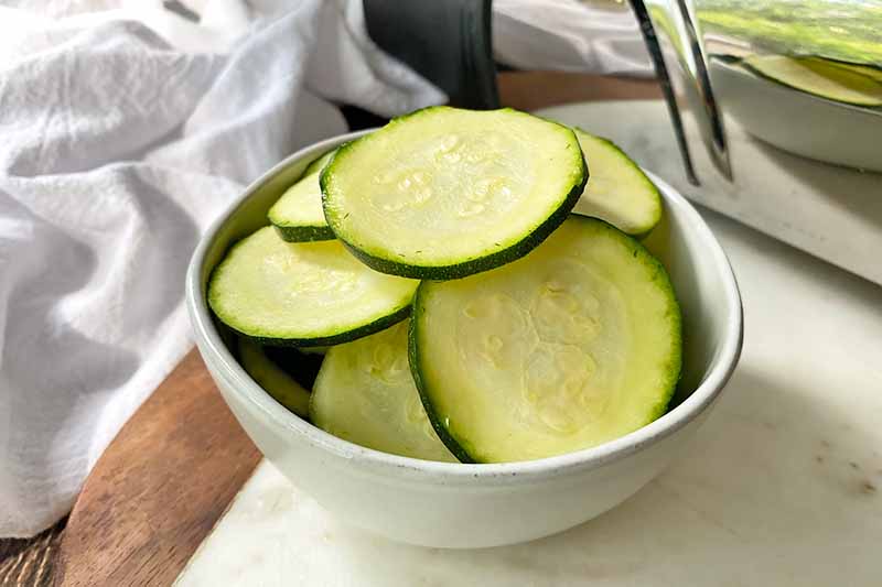 Horizontal image of finely sliced zucchini in front of a metal kitchen tool.