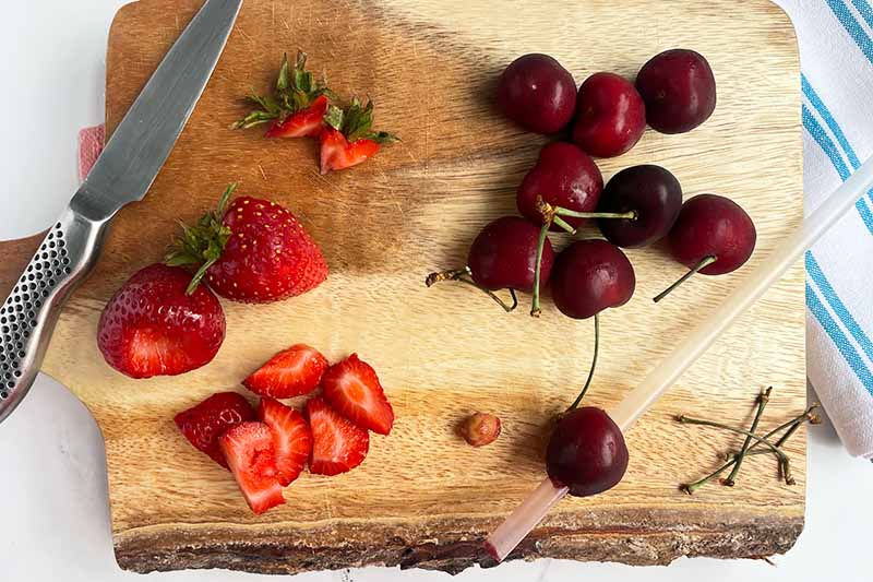 Horizontal image of prepping cherries and strawberries on a wooden cutting board.