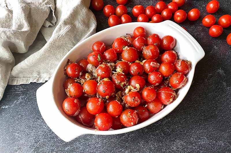 Horizontal image of seasoned tomatoes in an oval baking pan.