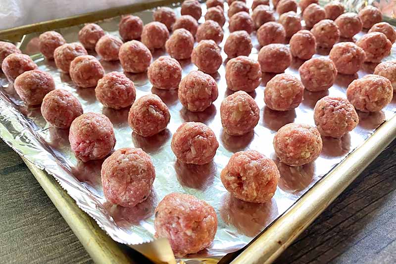 Horizontal image of raw mini meatballs on a lined baking sheet.