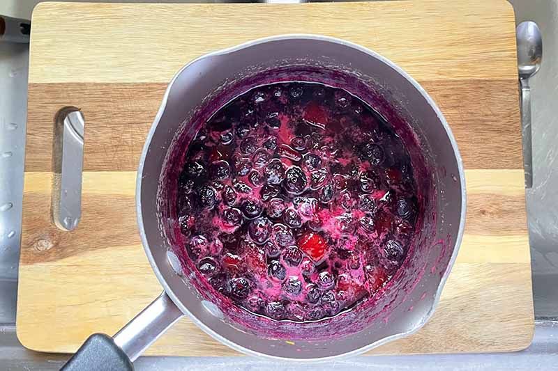 Horizontal image of a cooked blueberry liquid mixture in a small pot.