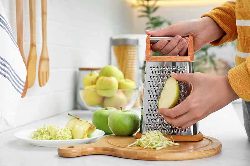 Horizontal image of grating fresh apples on the counter in a kitchen.