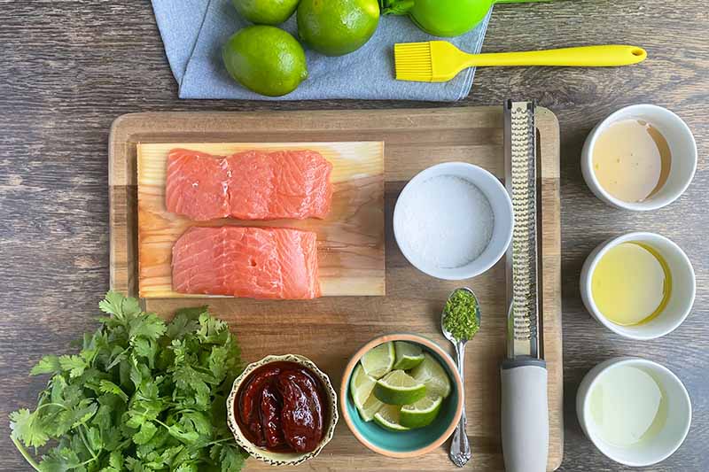 Horizontal image of prepped ingredients and pieces of fish on wooden boards.