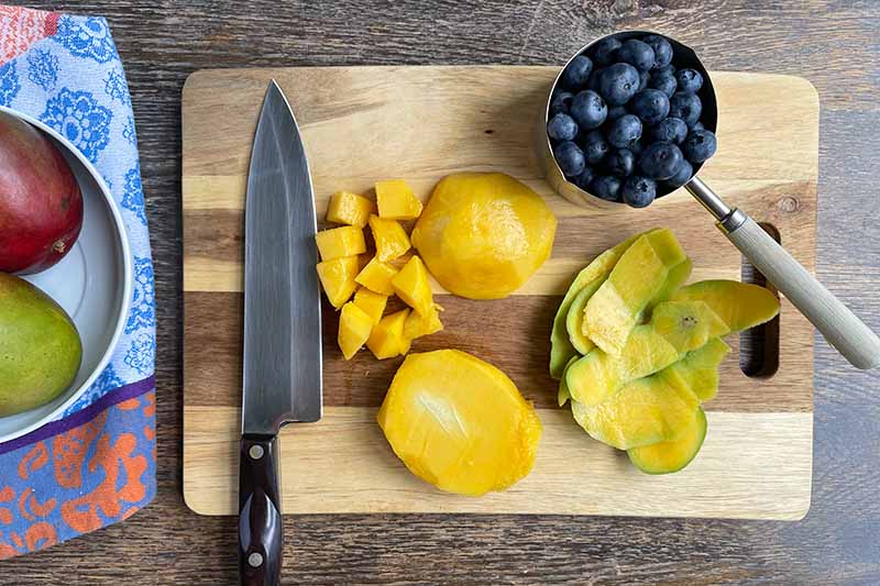 Horizontal image of prepped fruit on a cutting board next to a chef's knife.