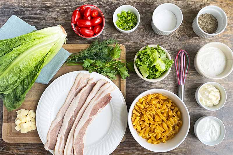 Horizontal image of an entire table of prepped ingredients, bacon, pasta, and produce.