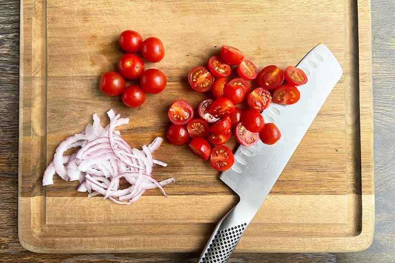 Horizontal image of sliced red onions and tomatoes on a wooden cutting board.