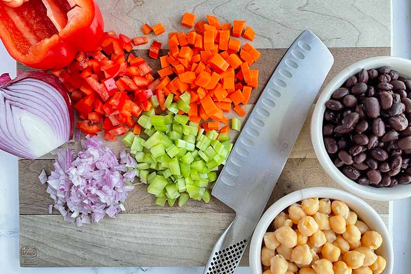 Horizontal image of diced assorted raw vegetables and beans in bowls.