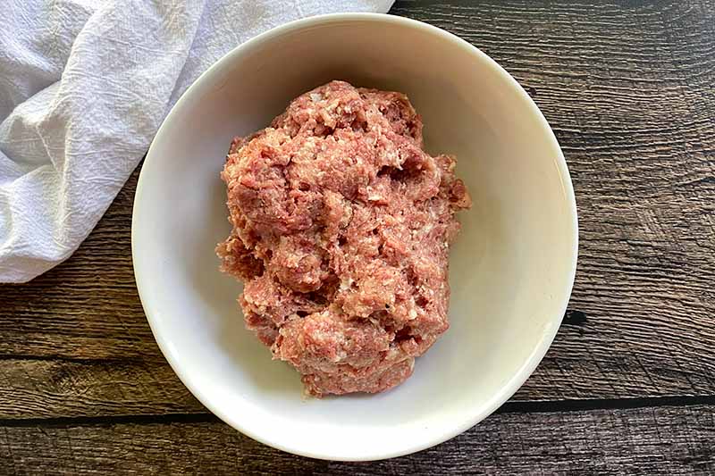 Horizontal image of a pile of ground beef and pork in a white bowl.