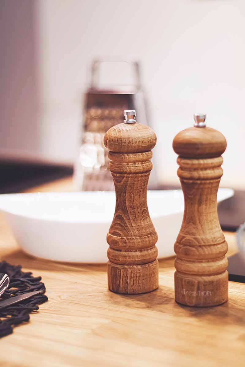 Vertical image of wooden kitchen gadgets next to a white bowl on a wooden table.