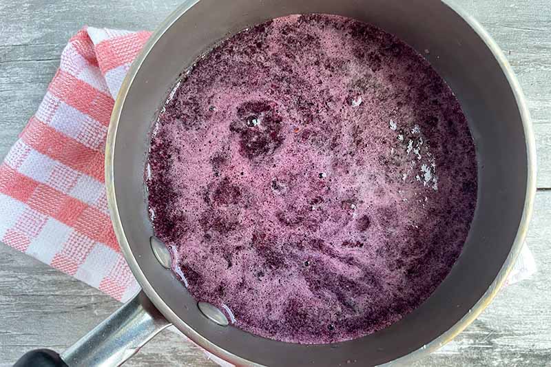 Horizontal image of cooking a dark purple liquid in a pot.