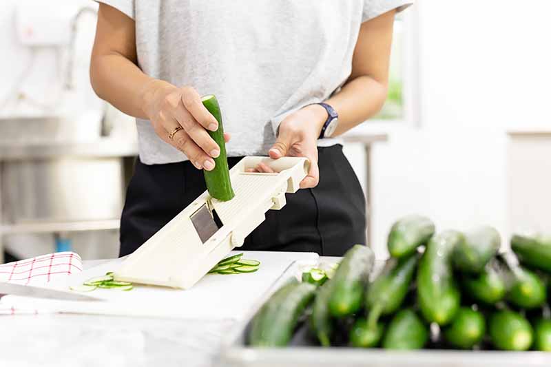 Horizontal image of a woman prepping cucumbers.