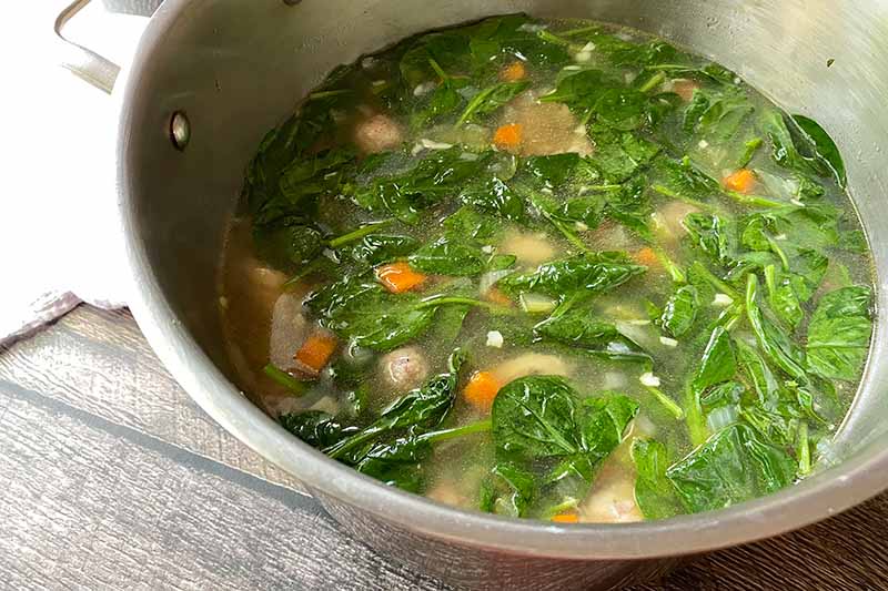 Horizontal image of spinach floating in a pot of stock.