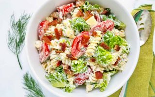 Horizontal top-down image of a large bowl filled with rotini, lettuce shreds, and sliced tomatoes on a green napkin.