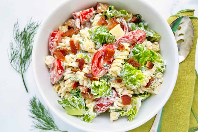 Horizontal top-down image of a large bowl filled with rotini, lettuce shreds, and sliced tomatoes on a green napkin.