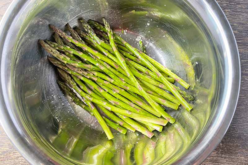 Horizontal image of lightly seasoned asparagus in a metal bowl.