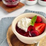 Horizontal image of a bowl filled with compote, whipped cream, and assorted fruit with a mint garnish.