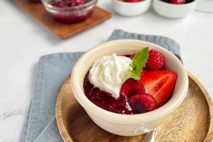 Horizontal image of a bowl filled with compote, whipped cream, and assorted fruit with a mint garnish.