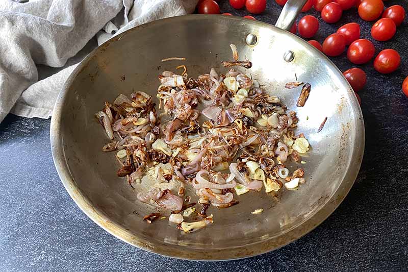 Horizontal image of cooked shallots and garlic in a pan.