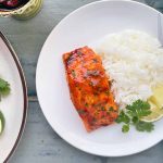 Horizontal image of white plates with seasoned and cooked fish fillets next to a bed of rice and herbs.