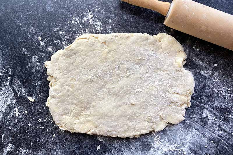 Horizontal image of a rectangle of dough on a lightly floured surface next to a wooden rolling pin.