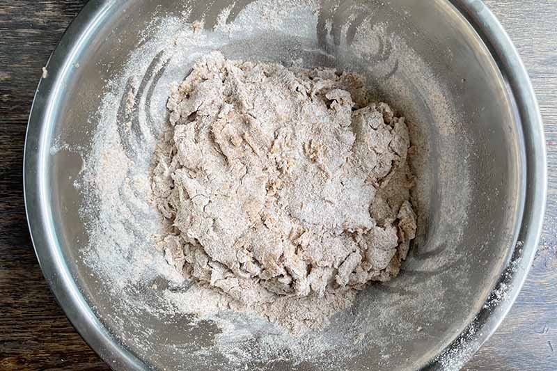 Horizontal image of a floured dough in a metal bowl.