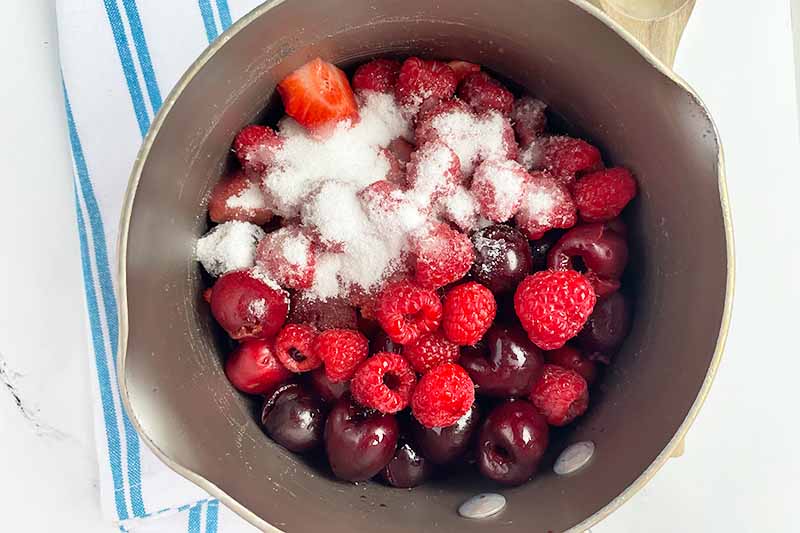 Horizontal image of cooking assorted fruit with sugar in a pot.