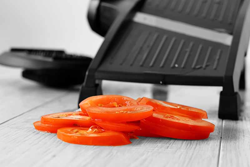 Horizontal image of cut fresh tomatoes in front of a black kitchen gadget.