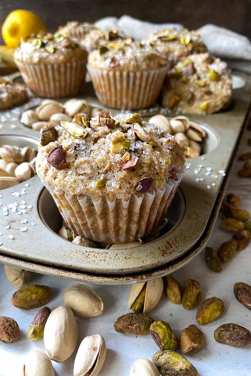 Vertical image of lined muffins topped with nuts and sugar on a metal tray.