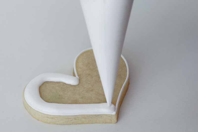 Horizontal image of piping icing on a heart-shaped dessert.