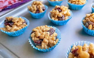 Horizontal image of portioned snack treats in mini blue paper liners on a baking sheet.