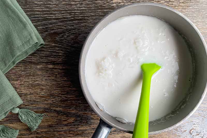 Horizontal image of mixing together milk and rice in a pot with a green spatula.