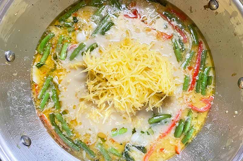Horizontal image of a mound of shredded yellow vegetables on top of a simmering broth in a bowl.