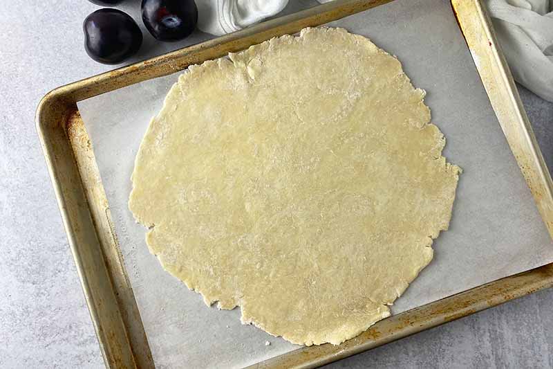 Horizontal image of a large flattened dough round on a baking sheet lined with parchment paper.