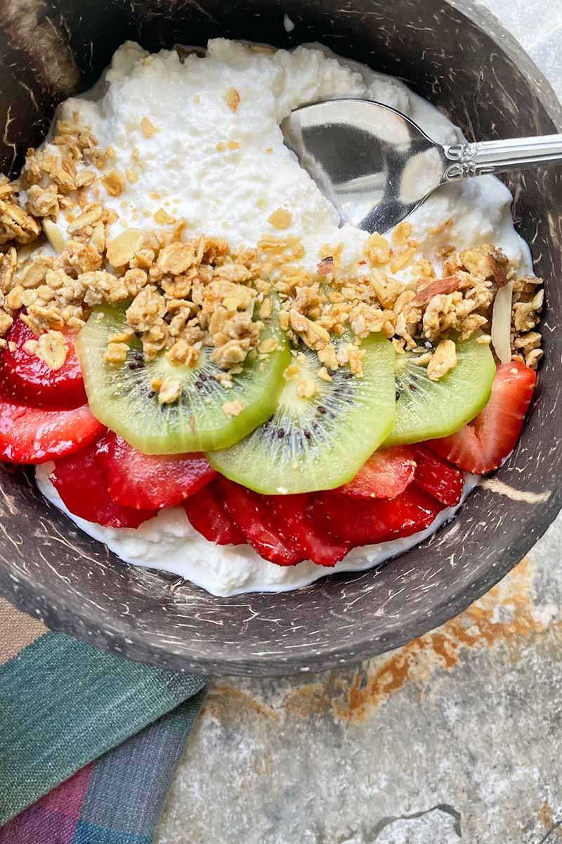 Vertical image of a wooden bowl filled with a bowl of sliced fruit and granola.