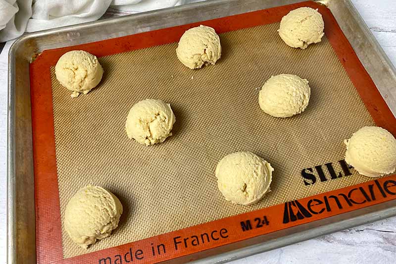 Horizontal image of portioned dough on a baking sheet lined with a silicone mat.