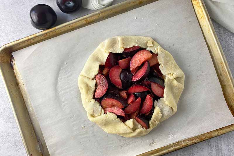 Horizontal image of an unbaked fruit crostata on a lined baking sheet.