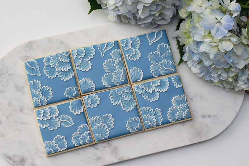 Horizontal image of brushed embroidery designs on square desserts on a marble slab.