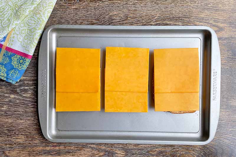 Horizontal image of slices of deli cheese on toast on a baking sheet.