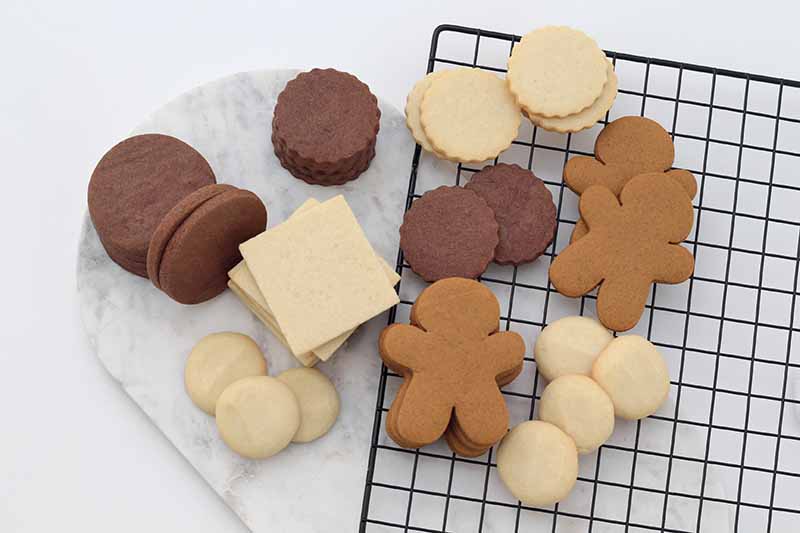 Horizontal image of assorted plain cookies on a marble slab and on a cooling rack.