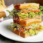 Horizontal image of a stacked vegetarian sandwich on a white plate on a wooden table.