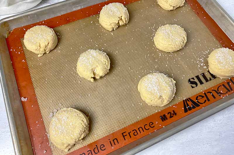 Horizontal image of portioned dough topped with sugar on a baking sheet lined with a silicone mat.
