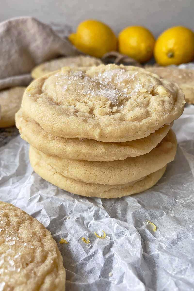 Vertical image of a stack of plain cookies on parchment paper in front of lemons and a tan towel.