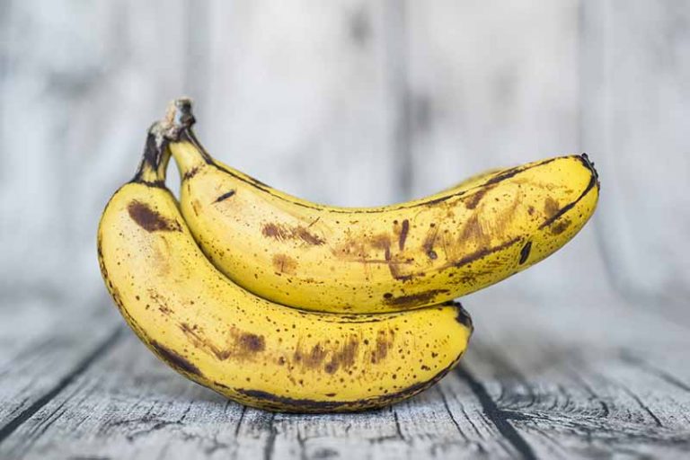 Horizontal image of two ripe bananas on a white wooden surface.