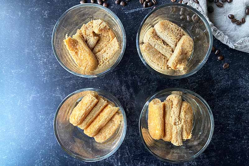 Horizontal image of a layer of soaked ladyfingers in four glass bowls.