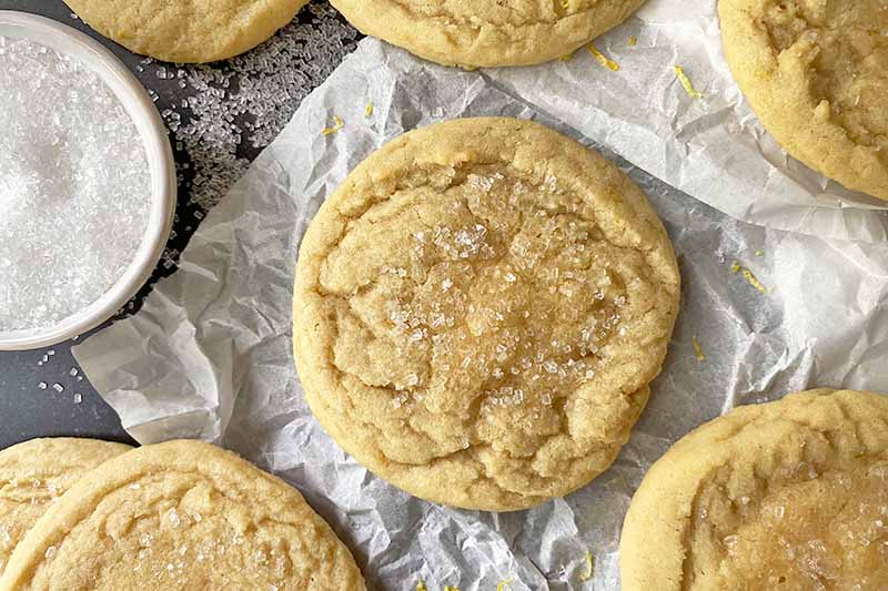 Horizontal top-down image of plain cookies with a crisp topping on a crinkled parchment paper piece.