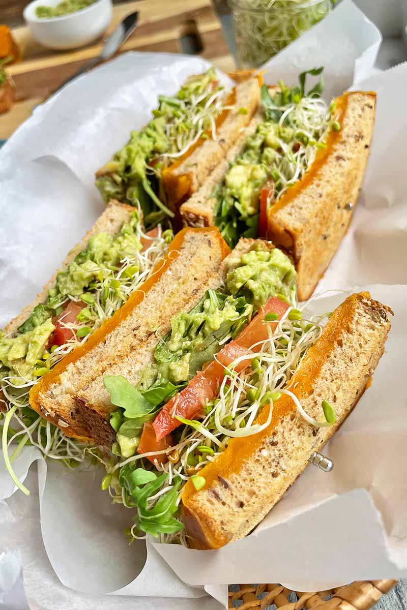 Vertical image of halved sandwiches with colorful fillings in a paper-lined basket.